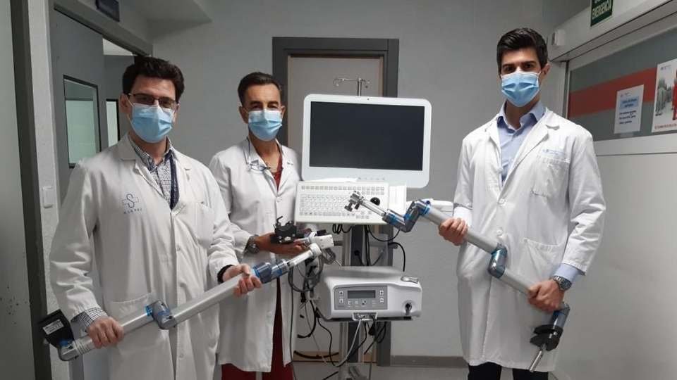 Tres urólogos con bata blanca y mascarilla junto a un equipo quirúrgico robótico en un hospital