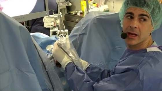 El Dr. Pérez-Carral, con gorro y bata quirúrgicos y un micrófono, explica una intervención en el quirófano