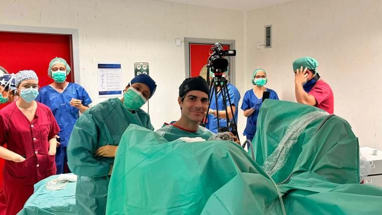 El Dr. Pérez-Carral, con pijama quirúrgico, sonríe a cámara en el quirófano con el equipo médico detrás