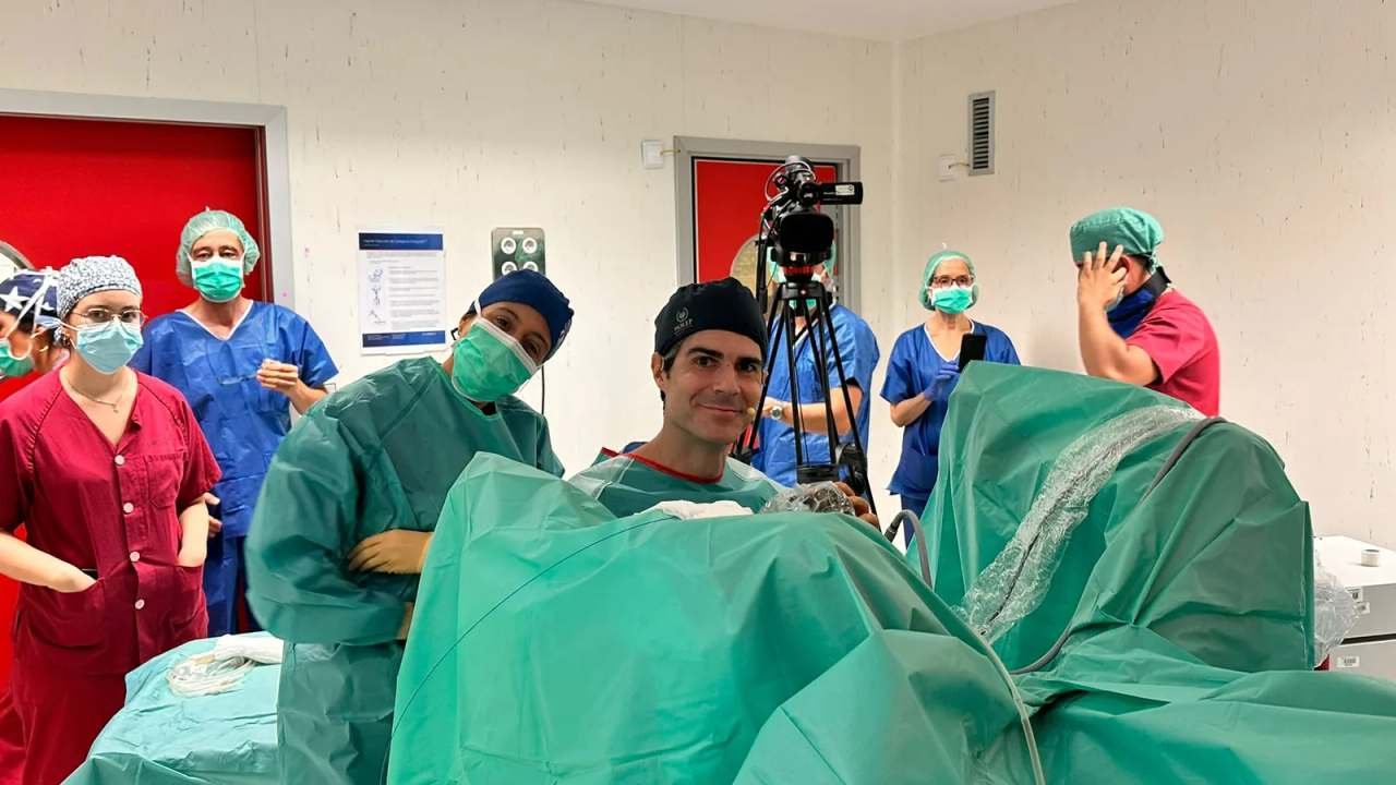 El Dr. Pérez-Carral, con pijama quirúrgico, sonríe a cámara en el quirófano con el equipo médico detrás